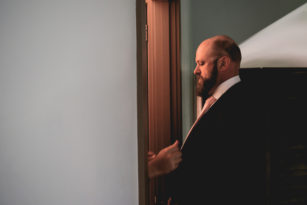 A groom adjusts his suit jacket in soft doorway light as he prepares for his Buttermilk Falls Inn wedding ceremony.