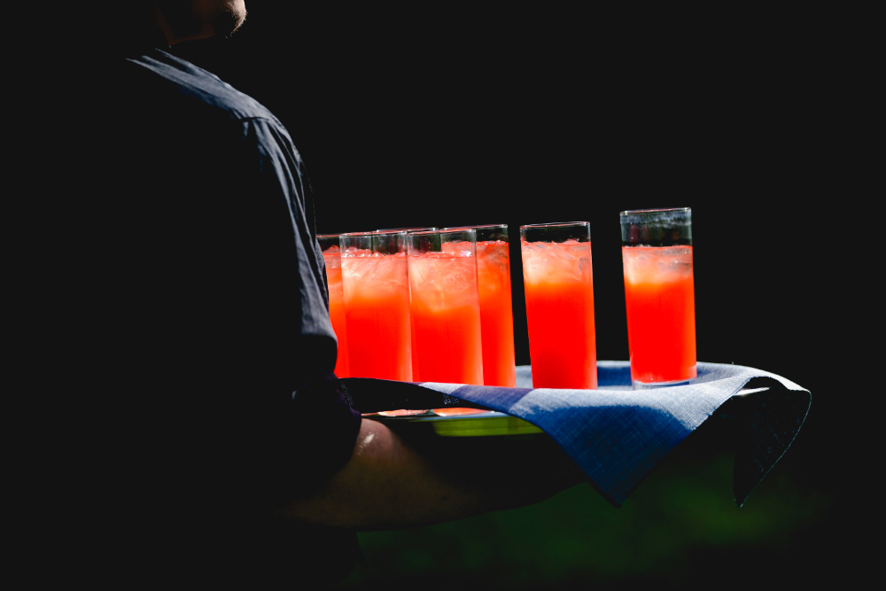 A server carries vibrant red signature cocktails on a tray during a Buttermilk Falls Inn wedding cocktail hour.