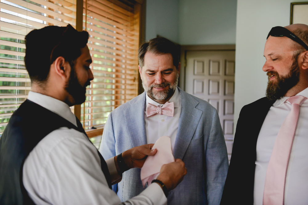 A groomsman folds a blush pocket square for one of the grooms during their Buttermilk Falls Inn wedding morning.