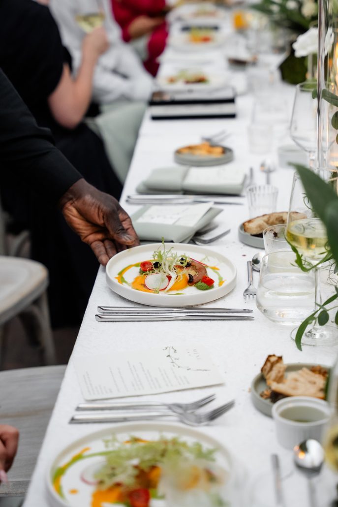 Servers presenting plated dinner courses under the tent