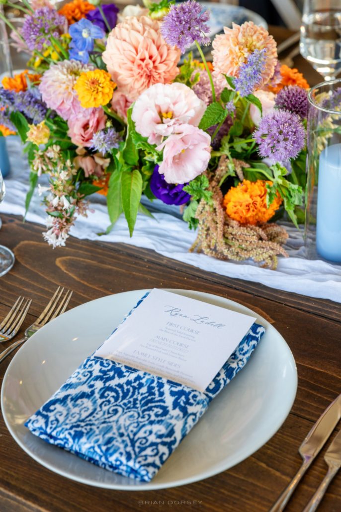 Bright and colorful floral arrangement with a patterned blue napkin and printed menu for a festive multi day wedding tablescape