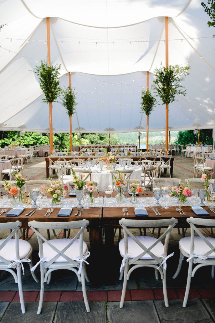 Tented wedding reception setup with long wooden tables, colorful florals, and mountain views as part of multi day wedding experiences.