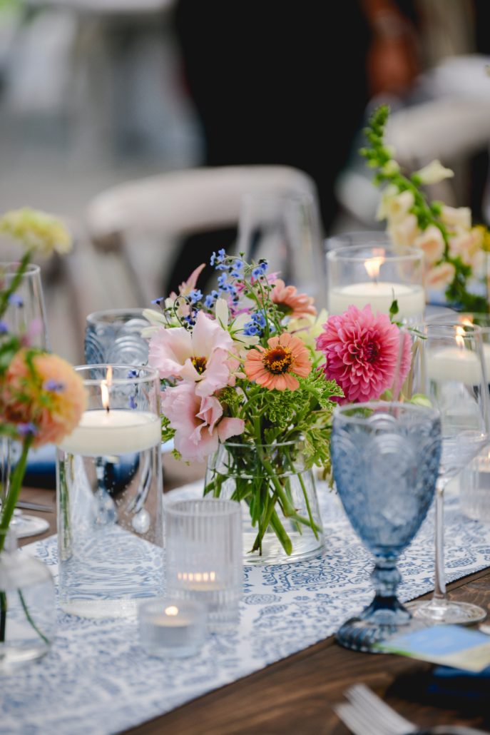 Close-up of bright floral centerpieces and candlelight on reception tables under a sailcloth tent.