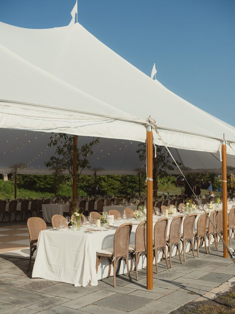Elegant tented reception setup with long tables, neutral linens, and natural wood chairs under a clear blue sky