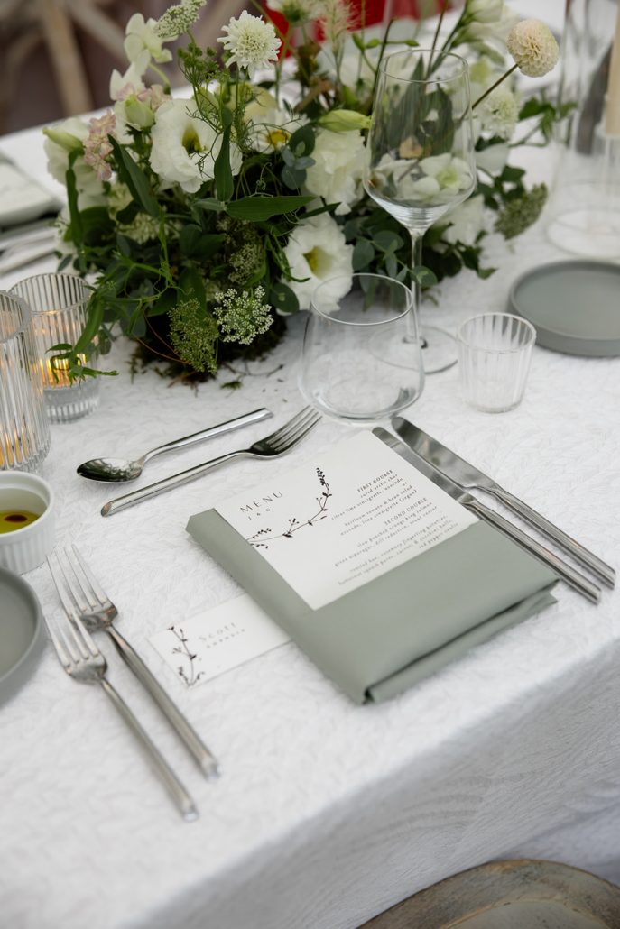 Refined table setting with sage green napkins, delicate florals, and modern glassware, perfect for a multi day wedding welcome dinner