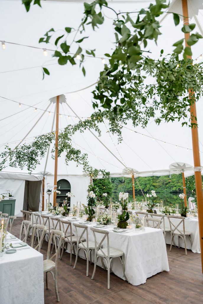 Tented reception filled with white linens, greenery installations, and soft candlelight reflecting over the lake