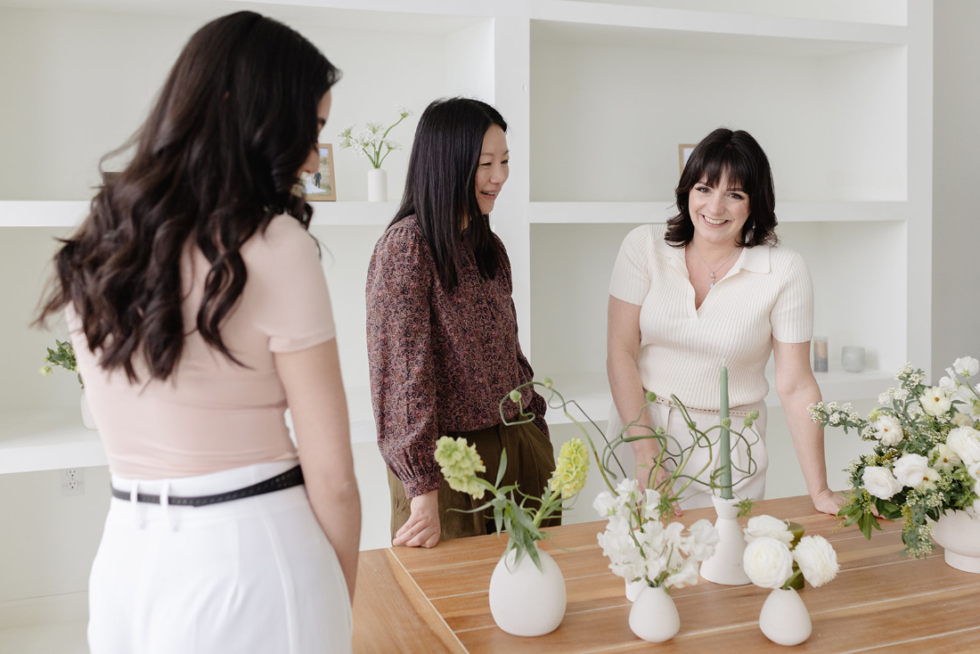 Three women discussing floral arrangements at a planning meeting with a full service wedding planner.