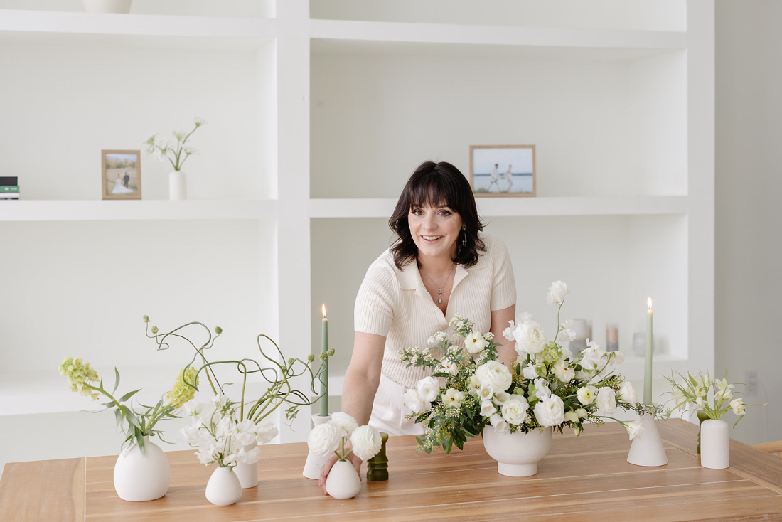 Full service wedding planner styling a table with elegant white floral arrangements and candles.