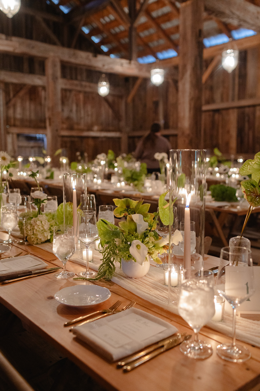 Rustic barn reception table designed by a full service wedding planner with candles and elegant green florals.