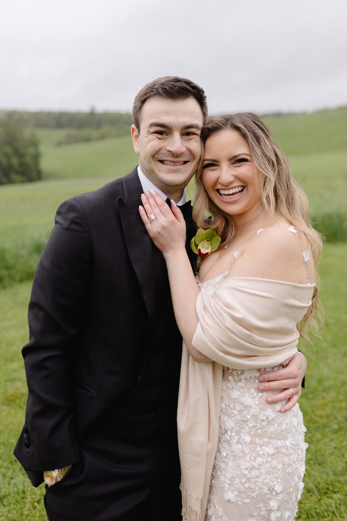 Bride and groom smiling in a scenic green field portrait during their elegant wedding weekend.