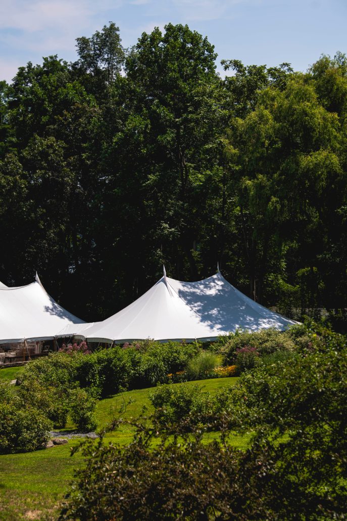 White sailcloth tent set in a lush garden landscape for an outdoor wedding weekend reception.