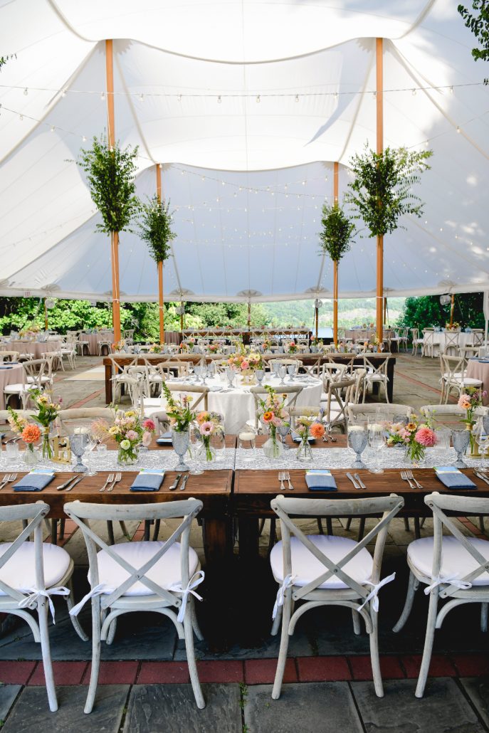 Floral-filled reception tables under a sailcloth tent designed for an elegant summer wedding celebration.
