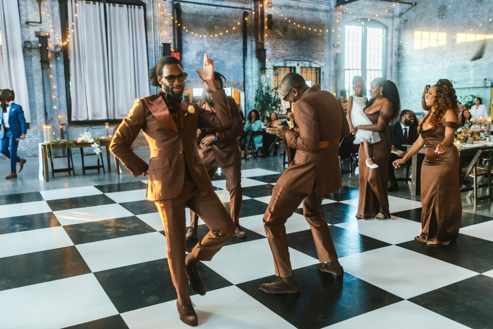 Groomsmen dancing on a black and white checkered floor during a lively wedding reception