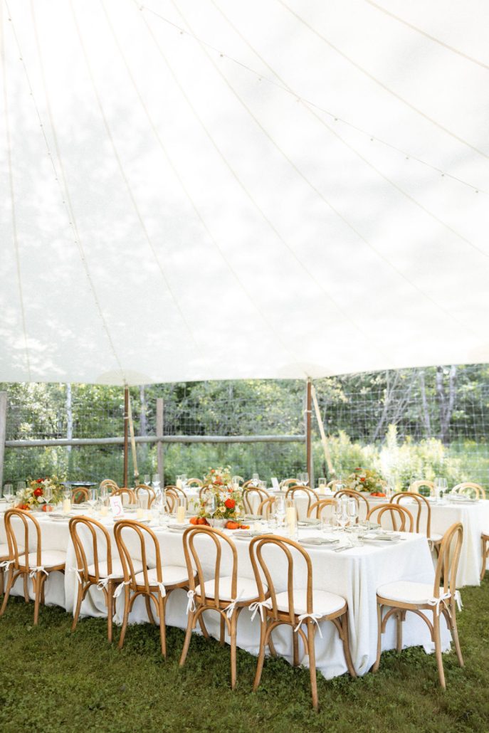 Elegant tented wedding reception with round tables, natural wood chairs, and refined place settings