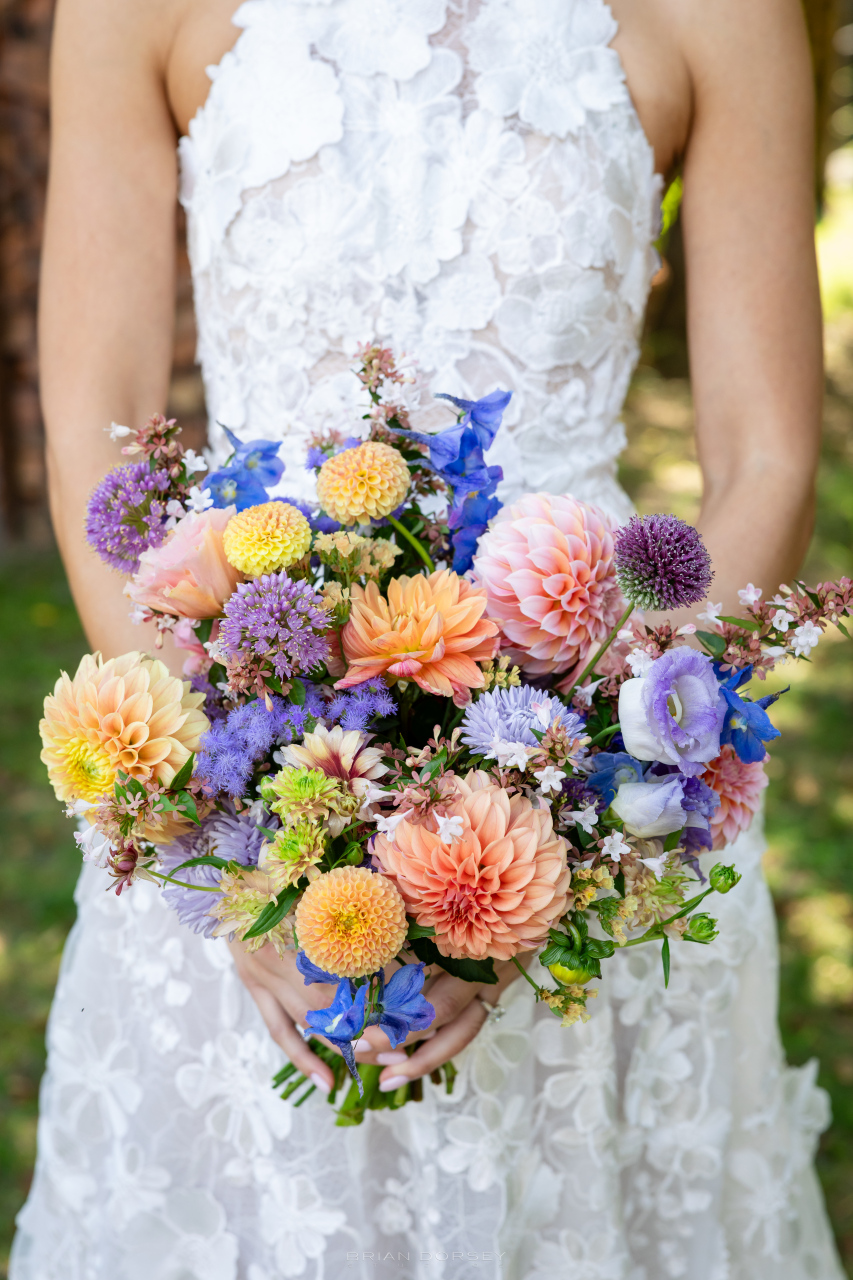Colorful bridal bouquet with seasonal blooms held against a textured lace gown in natural light