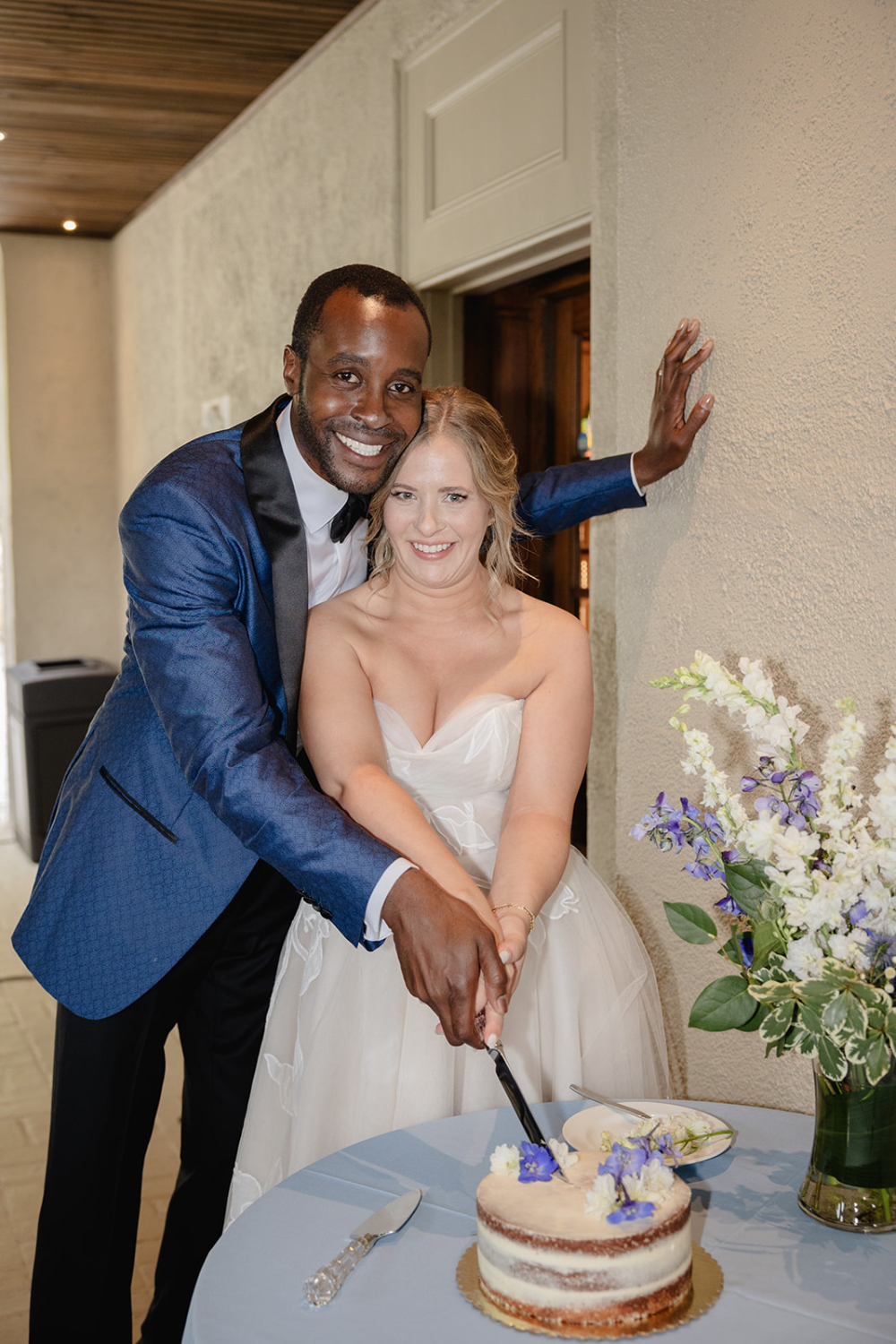 Couple cutting cake during an intimate indoor wedding reception with soft floral details