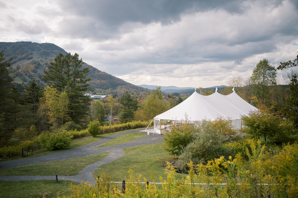 White sailcloth tent set on a scenic hillside with mountain views and dramatic clouds
