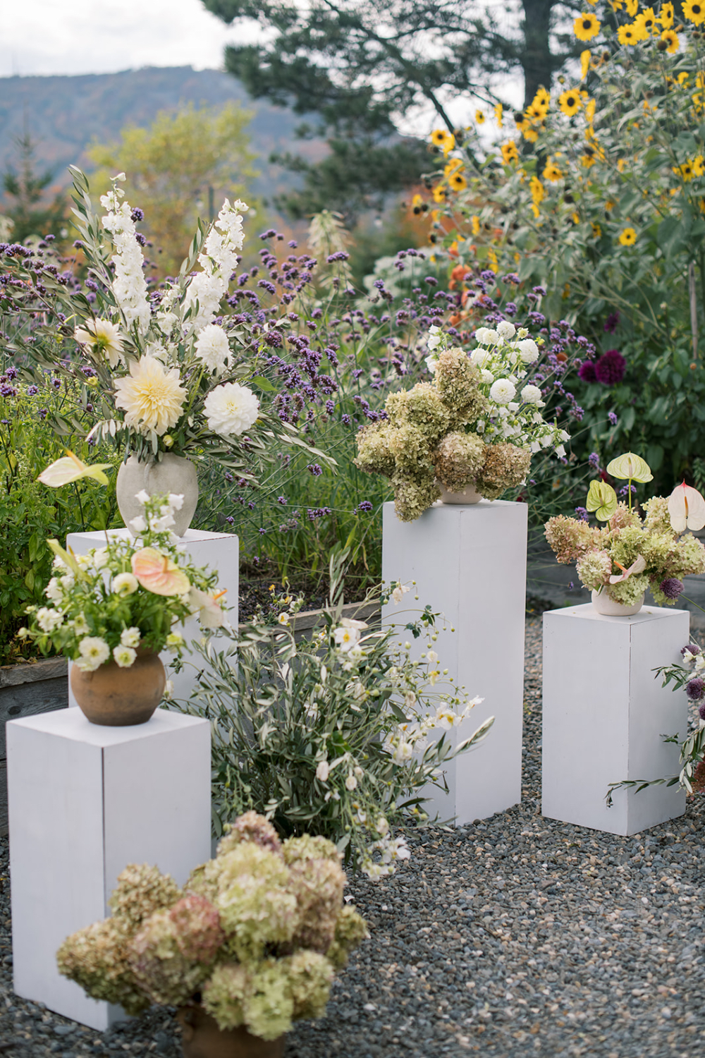 Garden-style floral arrangements on pedestal stands with seasonal blooms in an outdoor setting