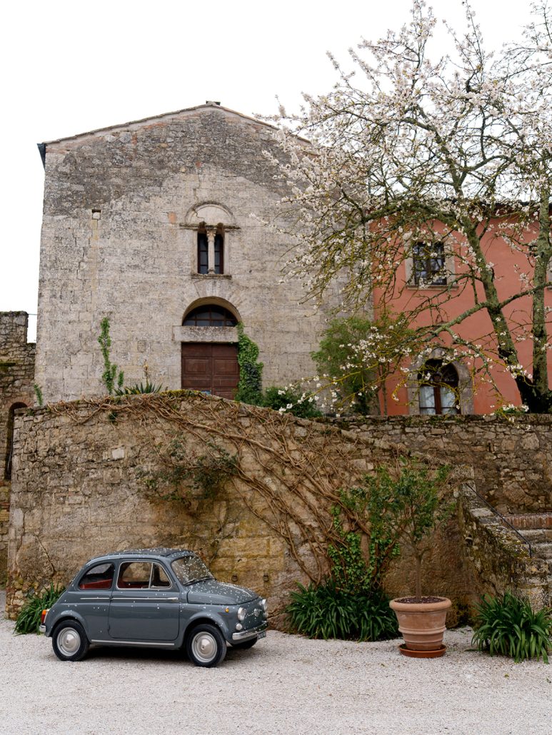 Vintage Fiat parked beside a historic stone chapel at a Tuscany destination wedding Italy venue.