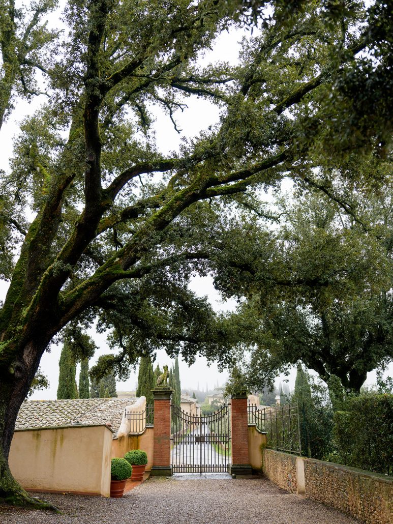 Private entrance framed by mature oak trees at a historic Tuscan wedding venue.