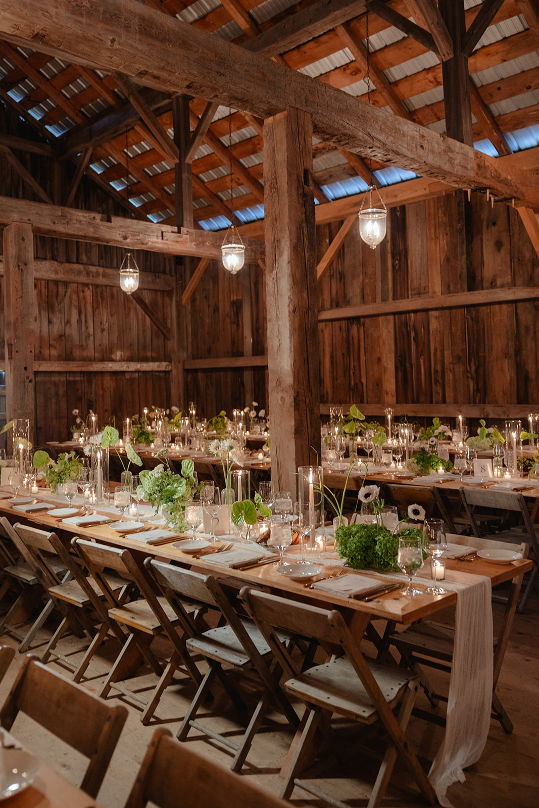 Rustic barn wedding reception with long farmhouse tables, candlelight, and lush greenery decor.