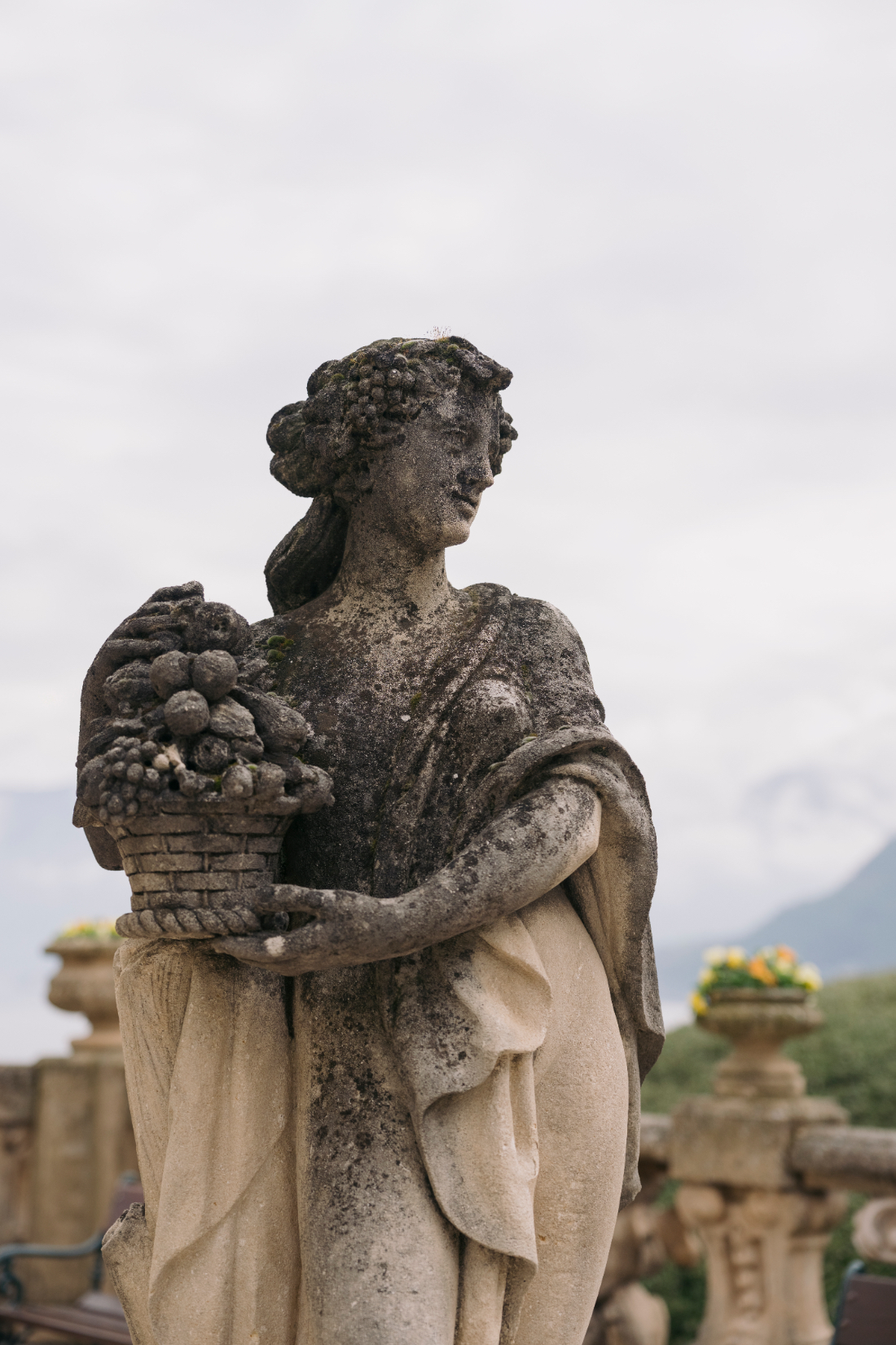Classical stone garden statue holding a basket of fruit overlooking the terraces at Villa del Balbianello wedding gardens.