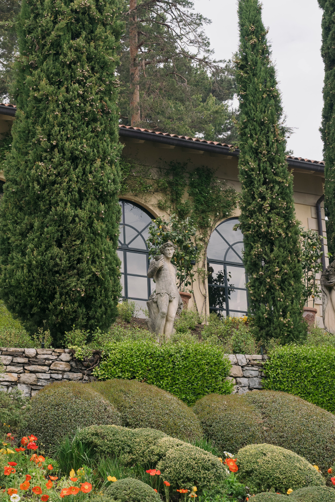 Manicured garden borders with statues, cypress trees, and colorful seasonal flower beds overlooking Lake Como.
