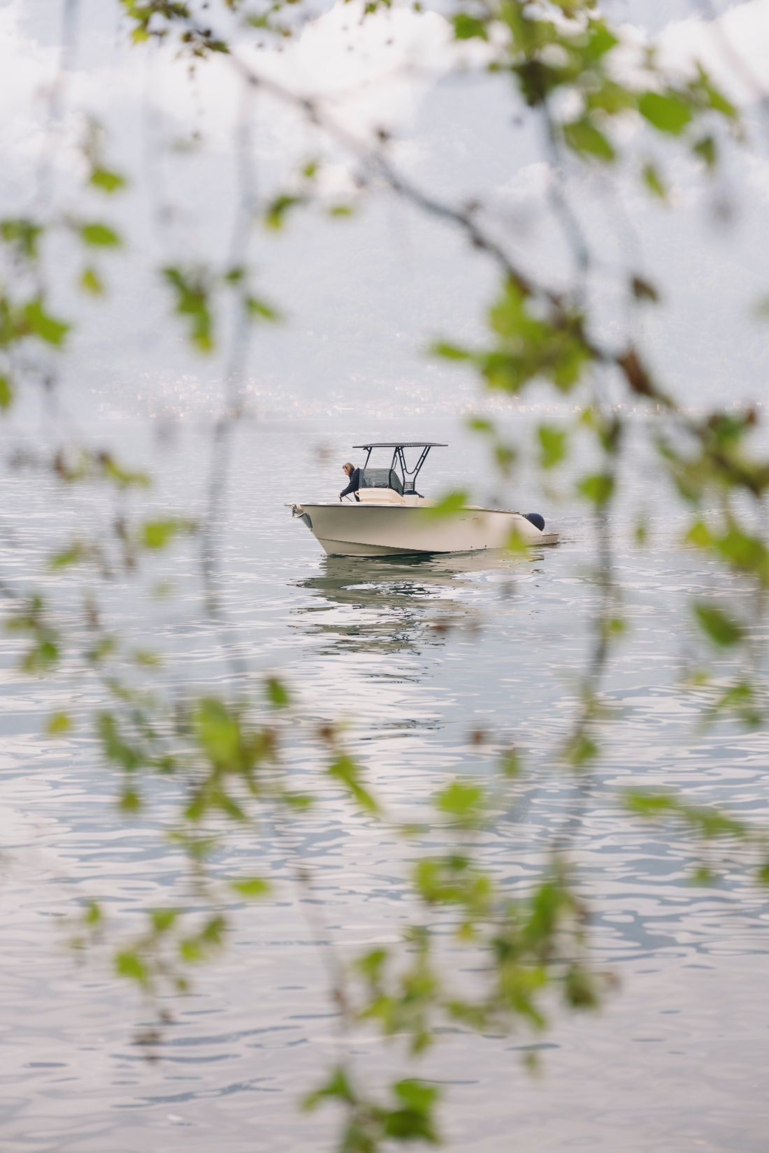Small motorboat gliding across the calm waters of Lake Como framed by fresh spring branches.