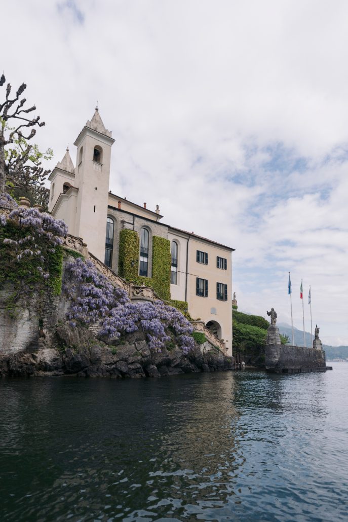 Historic bell tower, ivy-covered walls, and cascading purple wisteria overlooking the lake.