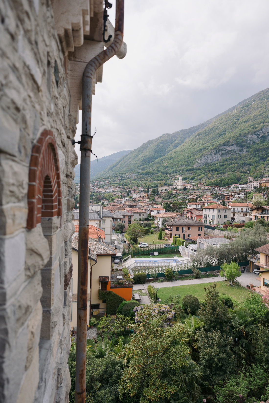 View from a historic villa across a charming Italian village nestled beneath lush green mountains near Lake Como.