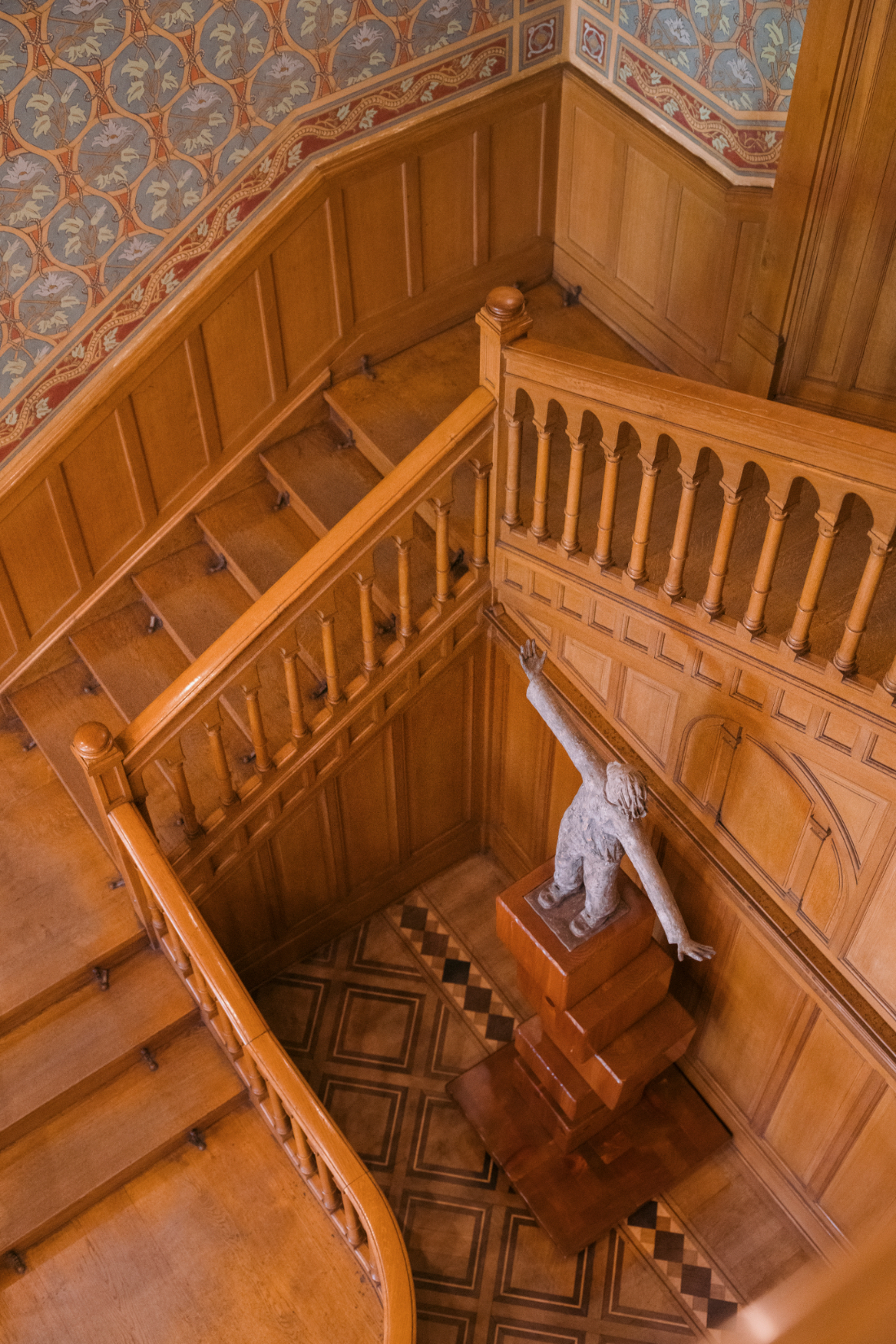 Curved wooden staircase with decorative wall murals and sculptural artwork inside an elegant historic Italian villa.