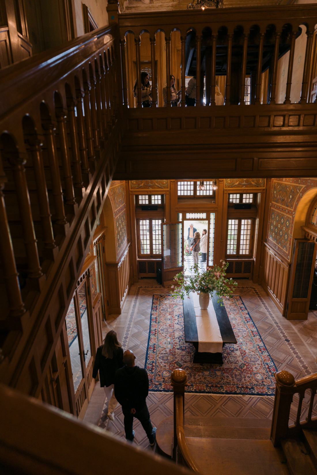 Grand entrance hall of a historic Italian villa featuring a sweeping staircase, patterned walls, and floral arrangement.