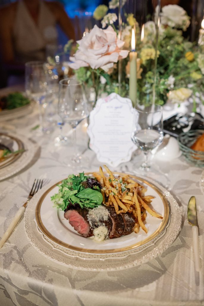 Luxury event planner candlelit dinner tablescape with garden florals, elegant china, steak frites, and custom menu card.