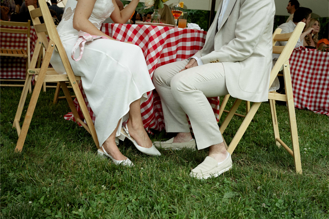 Newlyweds seated beneath a tent at an outdoor wedding reception with red gingham tablecloths